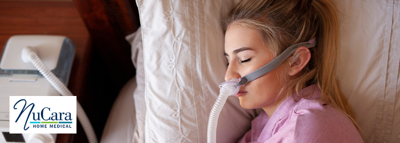 Woman sleeping on bed on her side with CPAP mask on and connected to a CPAP machine on the bedside table