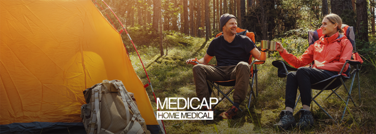 Image shows orange tent at left and two individuals sitting in lawn chairs in wooded environment
