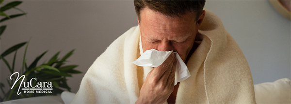 Man blowing his nose wrapped in a blanket because he has a cold
