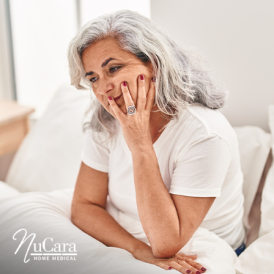 Older woman sitting up in bed with her hand on her face looking tired